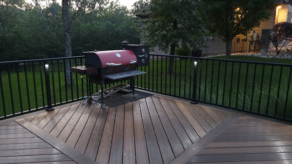 A BBQ grill sitting on a deck at dusk.