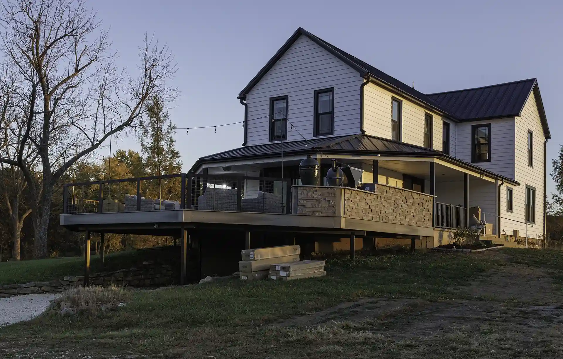 A large custom deck attached to a modern white house with stone accents, featuring a sleek railing and ample outdoor space.

