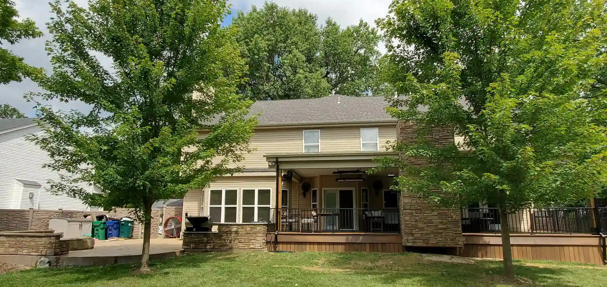 A large house with a deck, stone features, and trees in the yard.