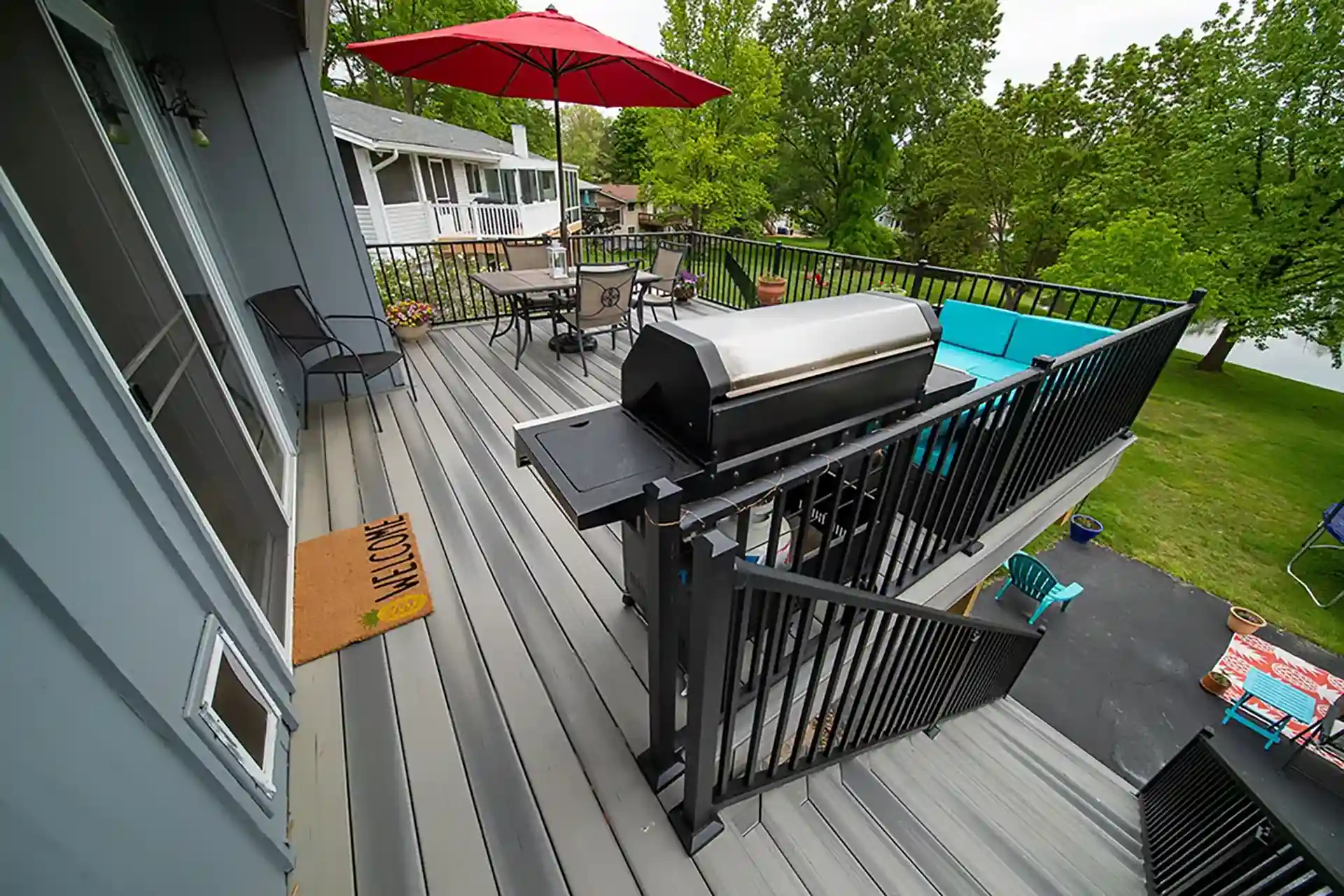 A composite deck featuring gray boards, black railings, and a grill area, with a dining set and colorful seating 