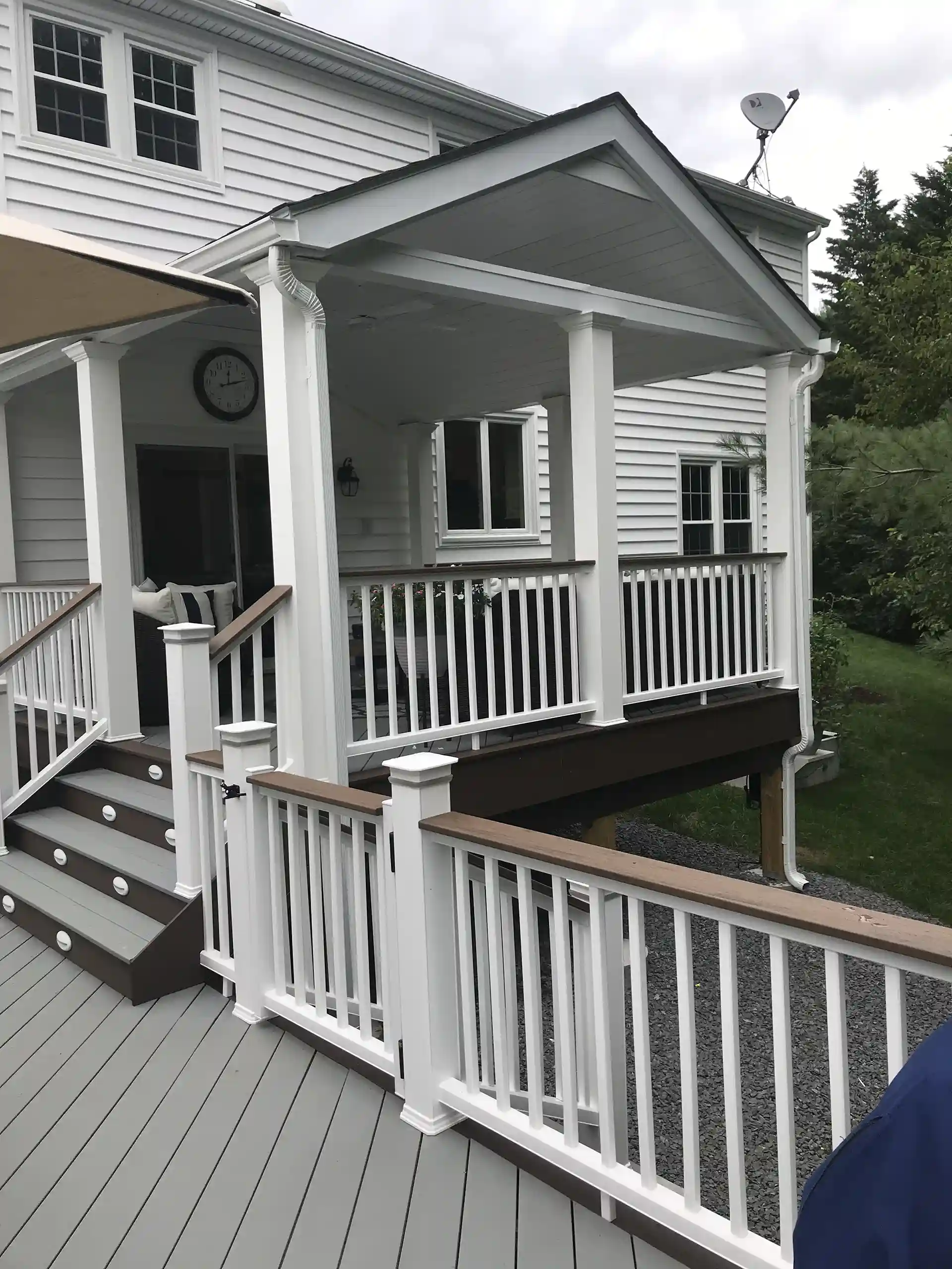 Patio cover with a solid roof over a deck, featuring white railings and stairs.