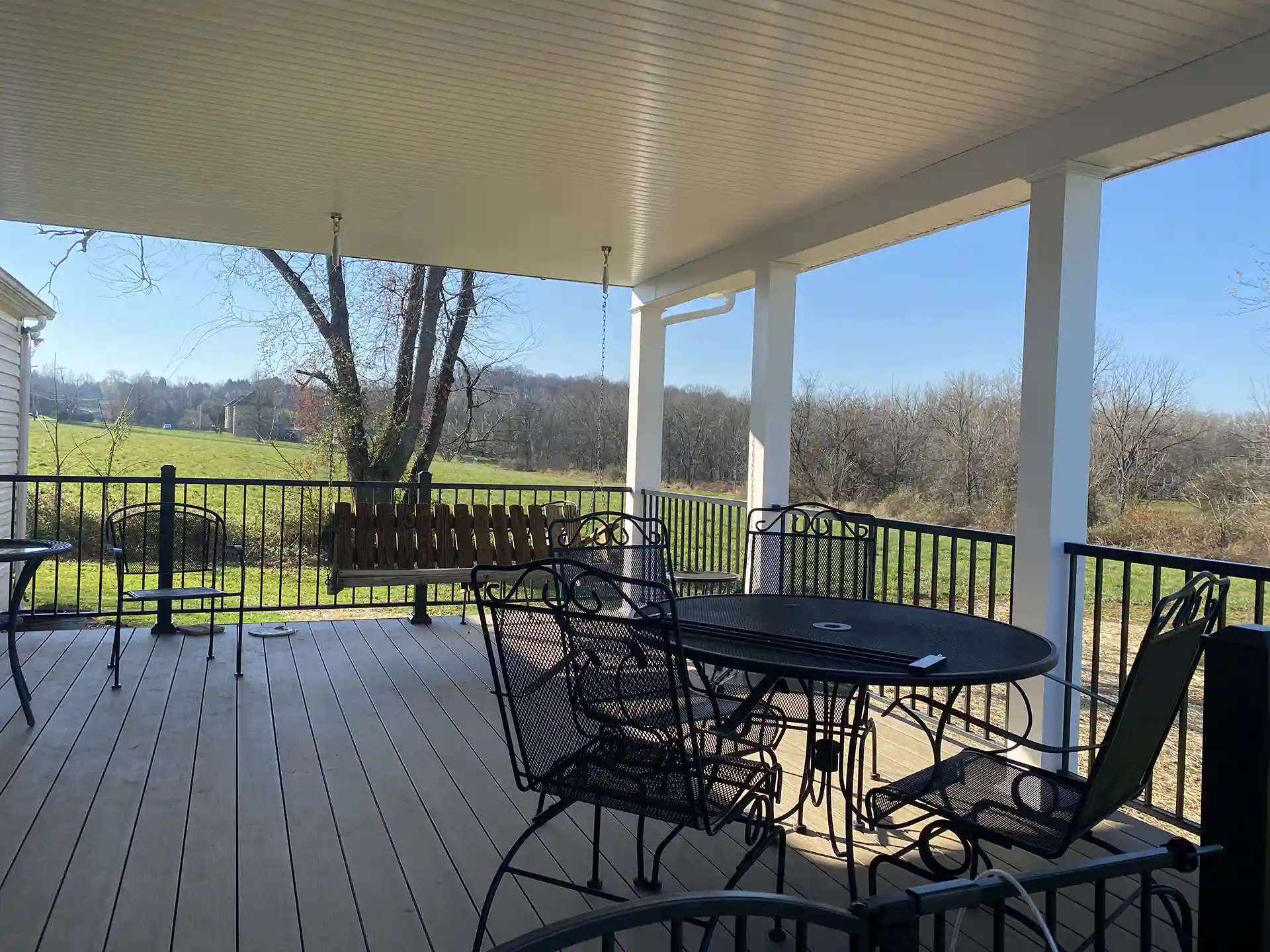 Patio cover with a solid roof over a deck, featuring metal railing and outdoor furniture.