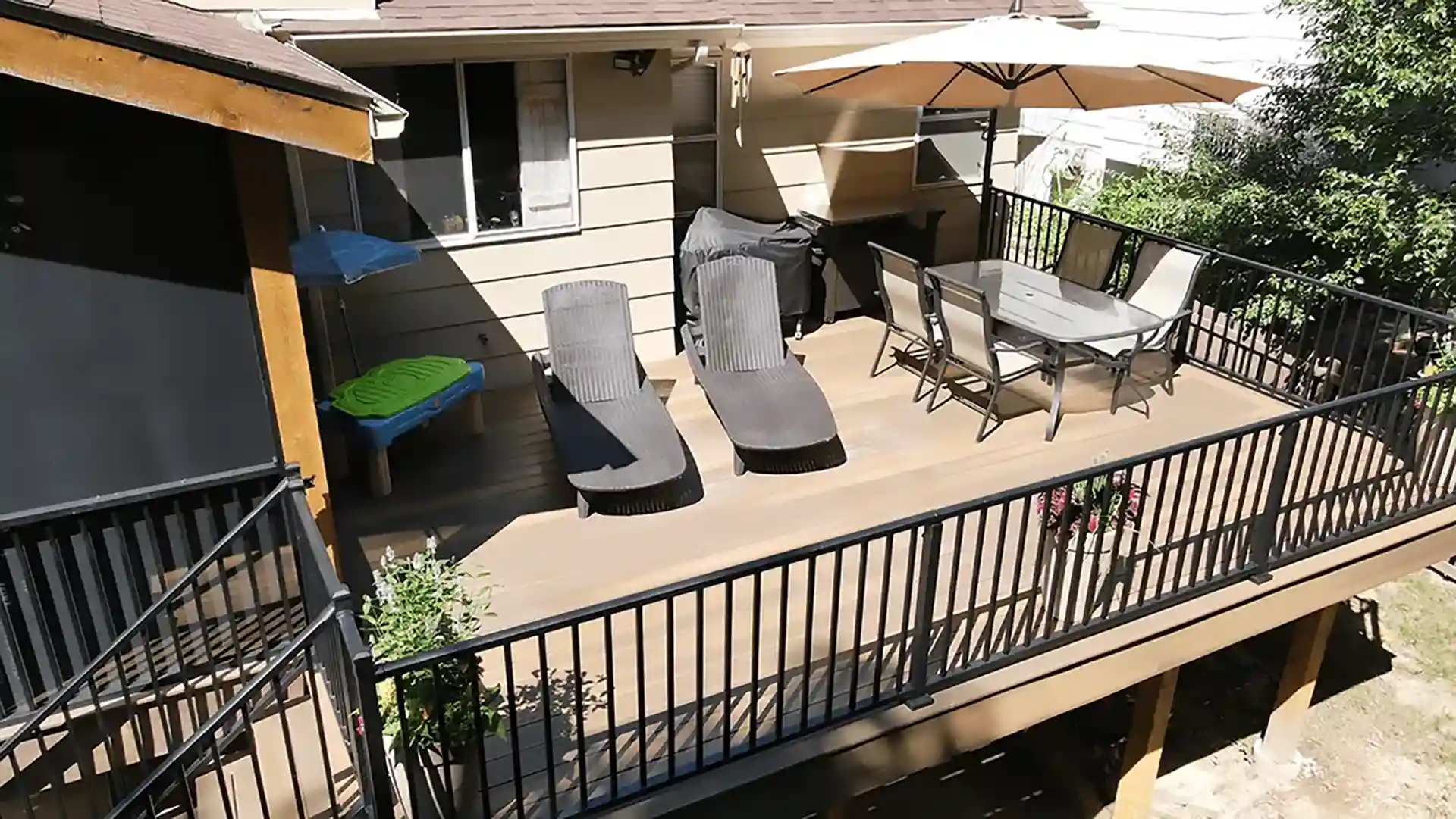 Elevated outdoor deck with composite flooring, lounge chairs, dining table, and a large umbrella providing shade.