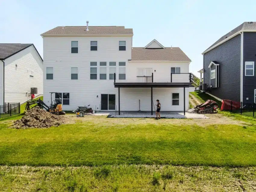 Photo of two-story white home with covered patio, construction equipment, and backyard lawn in progress.